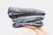 Young shopkeeper woman holding pile of jeans over light background in her hands