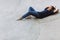 Young skater thoughtfully looking in camera while lying on skateboard in empty bowl at modern skatepark