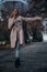 A young, slender, beautiful girl in a coat walks in the rain with a transparent umbrella in the park