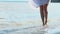 Young slender girl with bare feet walking model gait on sea sandy beach. Holding hands, white dress. surf hits woman on Shin and s