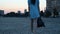 Young slender girl in a dress holding a backpack and walking down the street in the evening