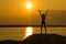 A young slender girl stands on top of a mountain holding her hands up towards the sun in the sunset.