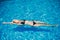 Young slender woman in a black bikini swimsuit relaxes on the surface of the water in the pool
