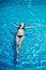 Young slender woman in a black bikini swimsuit relaxes on the surface of the water in the pool