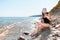 A young slender woman in black swimsuit smears sunscreen on the beach. The concept of protection from the sun and unwanted sunburn