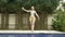 Young slender woman dances an oriental dance near pool in tropical resort