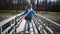 The young slender woman goes along the wooden bridge in the park in sunny day