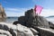 Young slender woman on the sea rocky shore in a pink swimming suit and a pink fabric fluttering in the wind.