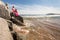 Young slender woman on the sea rocky shore in a pink swimming suit and a pink fabric fluttering in the wind.