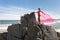 Young slender woman on the sea rocky shore in a pink swimming suit and a pink fabric fluttering in the wind.