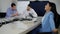 Young slim Asian woman stretching sitting in office as blurred Middle Eastern men talking at background. Side view