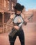Young slim attractive cowgirl gunfighter wearing gun belt and holding a rifle in an old western street. 3D illustration