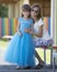 Young slim blond smiling mother, aunt or sister hugs small pretty preschool daughter girl in long nice blue evening dress on