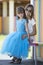 Young slim blond smiling mother, aunt or sister hugs small pretty preschool daughter girl in long nice blue evening dress on blur