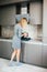 Young slim blonde woman in grey dress standing by the stove in the modern grey kitchen