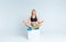 Young slim blonde woman in sportswear sitting on a white cube in studio in lotus position. Meditation, yoga, wellness concept