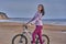 Young slim brunette woman on a bike ride on the sandy shore of a large river.