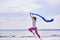 Young slim brunette woman jumping while jogging while holding a blue scarf in her hands. A woman is engaged in gymnastics in the s