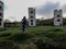 A young Slim girl with long blond hair stands on a vacant lot in front of three dilapidated towers on a cloudy day