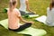 Young slim girl sits relaxing in the lotus position doing exercises on yoga mats with other girls on green grass in the
