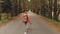 A young slim girl in a yellow hat and a vintage backpack walks along an asphalt road in the autumn yellow coniferous