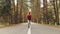 A young slim girl in a yellow hat and a vintage backpack walks along an asphalt road in the autumn yellow coniferous