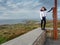 Young slim teenager tourist standing on a stone fence. One hand on Sky Road sign. Beautiful scenic background and blue cloudy sky