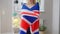 Young slim unrecognizable British woman wrapping in national flag and smiling standing at home. Cheerful proud Caucasian