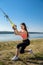 Young slim  woman doing suspension training with fitness straps outdoors near the lake at daytime. Healthy lifestyle