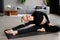 A young slim woman has done splits, and is stretching herself with her head and her hand up to her toes. Joyful talented woman