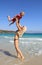 Young slim woman throws up and catches her little son on the beach by the clear blue sea. Mother and her cute little baby-boy are