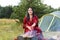 A young smart gypsy woman grills meat on the grill near the tent in the smoke of the fire.