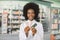 Young smiling African American woman pharmacist holding different colorful medicines blisters in hands, while standing
