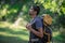 Young smiling backpack man in summer forest nature. Happy handsome male adult student looking at camera walking hiking in forest