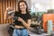 Young smiling barista woman pouring whipped milk into coffee drink, preparing latte macchiato, looking happy