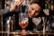 Young smiling barman stirring fresh alcoholic cocktail with syrups