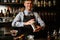 Young smiling bartender holds in his hands steel shaker and empty glass