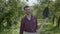 Young smiling bearded farmer walking through the garden with a shovel and pitchfork in hands. Concept of rural life