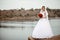 A young smiling and beautiful bride in a white dress is standing against a background of rocks, cliffs and stones.