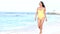 Young smiling beautiful woman in a swimsuit walks along the sea coast. Summer vacation at the sea. Azure waves