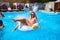 Young smiling bikini girl having fun with friends on inflatable swan in swimming pool. Happy people splashing water on