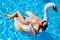 Young smiling blonde girl in bikini relax chilling on an inflatable swan in swimming pool. Attractive woman in swimwear