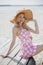 Young smiling blonde girl look like a Barbie doll in pink mini dress and wide brim hat sitting on beach