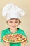 Young smiling boy in chefs hat with cooked homemade pizza