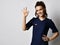 Young smiling brunette woman doctor gynecologist in blue dress standing and showing ok good sign with fingers