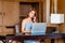 Young smiling business woman using laptop computer, calling by phone in modern apartment. Attractive businesswoman