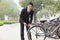 Young smiling businessman locking up his bicycle on a city street in Beijing, looking at camera