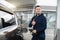 Young smiling Caucasian man refuelling his modern car at a petrol station, posing to camera with his thumb up