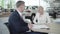 Young smiling Caucasian woman passing business card to adult man in car dealership. Trader and client shaking hands in