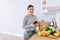 Young smiling caucasian woman use smartphone in the modern kitchen, bag with fresh vegetable on the table. Online buying food and